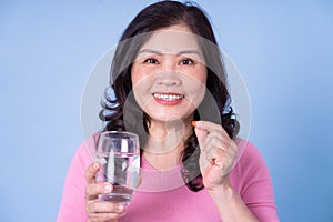 Image of middle aged Asian woman using pill on blue background