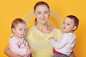 Image of mother with kids, two daughters in casual clothes, beautiful young woman with little twins standing in photo studio