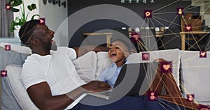 Image of network of connections over happy african american father and son using laptop