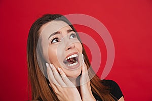 Image of neurotic woman 20s in black t-shirt screaming and looking up with fright, isolated over red background