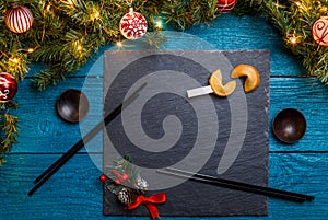 Image of New Year branches of fir, black board, sticks for sushi, cookies with prediction