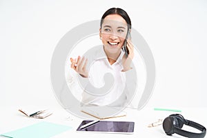 Image of office employee, asian woman in office talks on mobile phone, discusses work on cellphone, white background