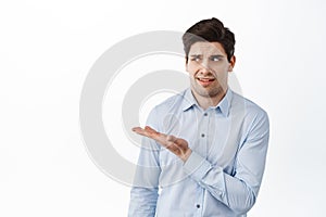 Image of office worker, businessman in shirt pointing, looking aside at something strange, standing confused and