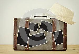 Image of old vintage luggage, fedora hat and blank photos for photography montage mockup over wooden floor.