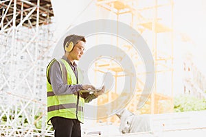 Image outside the industrial construction engineers in yellow protective ear muff discuss new project while using laptop