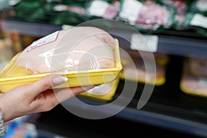 Image of packaged hen meat with woman hand in the supermarket