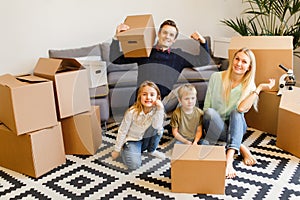 Image of parents with children sitting on floor among cardboard boxes