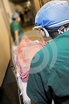 Image with perspective of following Medical Professionals in green scrubs pushing a gurney down hospital hallway