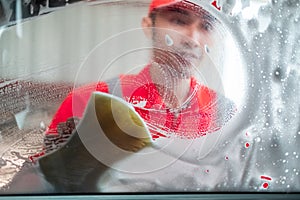 Image photo from inside the car cleaning car Asian man wearing uniform cleaning the side glass with a foamy sponge