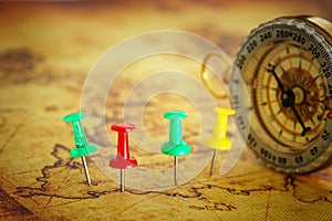 Image of pins attached to map, showing location or travel destination over old map next to vintage compass. selective focus.