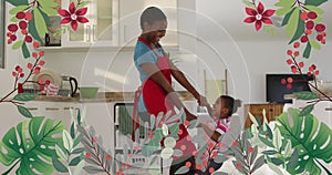 Image of plants and flowers over happy african american mother and daughter dancing in kitchen