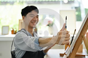 Image of pleased man artist painting picture with watercolor on canvas in art workshop. Art, creative hobby and leisure