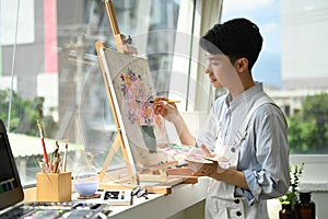 Image of pleased man artist painting picture with watercolor on canvas in art workshop. Art, creative hobby and leisure