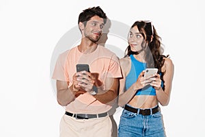 Image of pleased young couple smiling while using cellphones