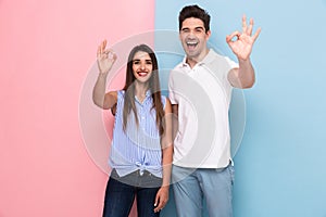 Image of positive couple in casual t-shirts smiling and gesturing ok sign, isolated over colorful background