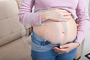 Image of pregnant woman touching her belly with hands at home. Copy space and mock up. Cropped image