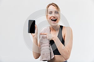 Image of pretty blond woman 20s dressed in sportswear with towel over neck using smartphone during workout in gym