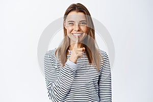 Image of pretty blond woman shushing and smiling, making shh taboo gesture and looking at camera, asking to keep quiet