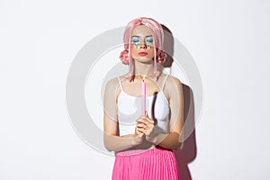 Image of pretty girl in pink wig, with bright makeup, dressed up as fairy for halloween party, close eyes while holding