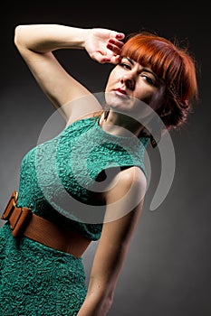Image of pretty redhead young lady in green dress standing with arms crossed over grey wall background. Looking camera.