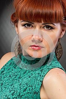 Image of pretty redhead young lady in green dress standing with arms crossed over grey wall background. Looking camera.