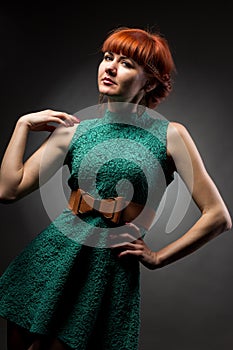 Image of pretty redhead young lady in green dress standing with arms crossed over grey wall background. Looking camera.