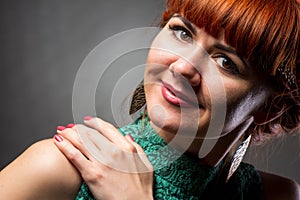 Image of pretty redhead young lady in green dress standing with arms crossed over grey wall background. Looking camera.