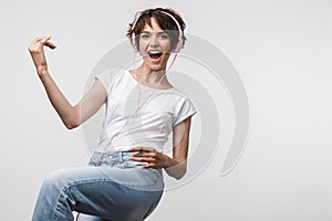 Image of pretty woman in basic t-shirt playing invisible guitar while listening to music with headphones