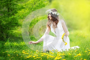 Image of pretty woman in a white dress weaves garland from dandelions in the field, happy cheerful girl resting on dandelions me