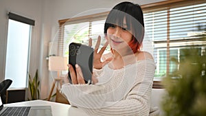 Image of pretty young asian woman waving hand, making video call, chatting online on mobile phone