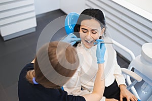 Image of pretty young woman sitting in dental chair at medical center while professional doctor checks her teeth.