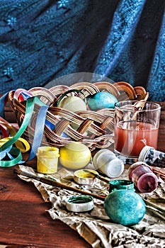 Image of the process of coloring Easter eggs at home. Easter. Eggs in a basket and colored paints on a wooden table.