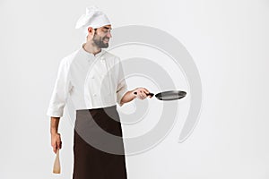 Image of professional chief man in cook uniform holding wooden kitchen spatula and frying pan