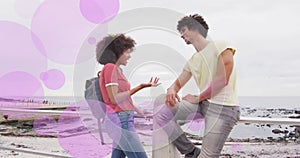 Image of purple spots over happy biracial couple talking on beach promenade