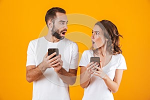 Image of puzzled couple man and woman using smartphones together, isolated over yellow background