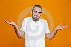 Image of puzzled man 30s in t-shirt throwing up hands,  over yellow background