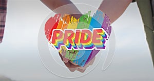 Image of rainbow heart and pride over hands of caucasian lesbian couple