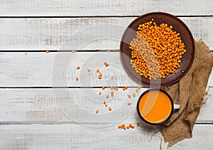 Image of raw sea buckthorn in a ceramic bowl and a cup of hot seabuckthorn tea on rustic wooden backgroud. Autumn backdrop.