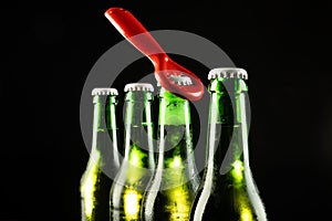 Image of red bottle opener and four green beer bottles with crown caps, with copy space on black