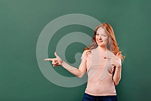 Image of a red-haired woman in casual wear smiling and pointing finger at copyspace