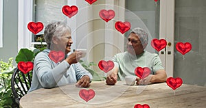 Image of red hearts over senior couple drinking coffee at home