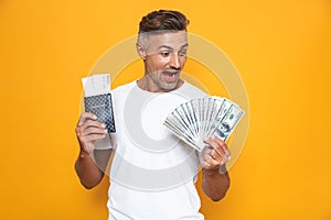 Image of rich man 30s in white t-shirt holding money fan and travel tickets