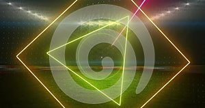 Image of rotating neon shapes and lights over floodlit sports field