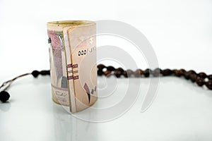 Image of saudi riyal banknote in SR100 denomination over reflective white. Focus on banknotes. Praye beads in visibility
