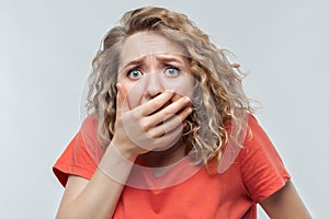 Image of scared blonde girl covering her mouth with hands. Fright, phobia and facial expression concept