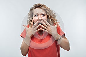 Image of scared blonde girl covering her mouth with hands. Fright, phobia and facial expression concept