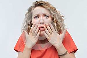 Image of scared blonde girl covering her mouth with hands. Fright, phobia and facial expression concept