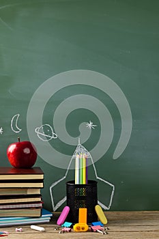 Image of school supplies, apple and notebook over drawings on black board