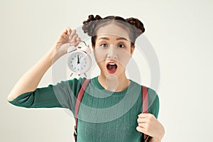 Image of screaming young confused woman standing isolated over white background. Looking aside holding alarm clock