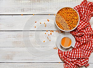 Image of sea buckthorn in a ceramic bowl and a cup of hot tea on a rustic wooden background. Autumn background. Immunization